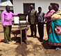 Vodilni člani zadruge Usongwe in naprava za ročno čiščenje kavnih češenj